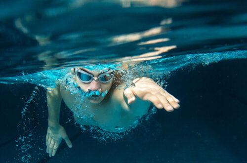Schwimmer unter Wasser mit Schwimmbrille, der in einem Pool in der Brustlage schwimmt, umgeben von sprudelndem Wasser.