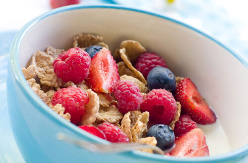 Schüssel mit Haferflocken, frischen Himbeeren, Erdbeeren und Heidelbeeren auf einem hellblauen Tisch. Gesundes Frühstück mit Obst und Müsli.