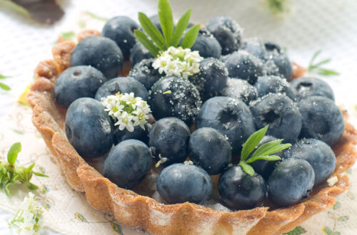 Frischer Heidelbeerkuchen mit Zucker und essbaren Blüten, auf einem dekorativen Serviette präsentiert.