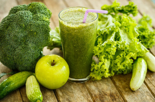 Grüner Smoothie aus Brokkoli, Gurken, grünem Apfel und Salat, umgeben von frischen Zutaten auf einem Holztisch. Ideal für eine gesunde Ernährung und reich an Vitaminen.