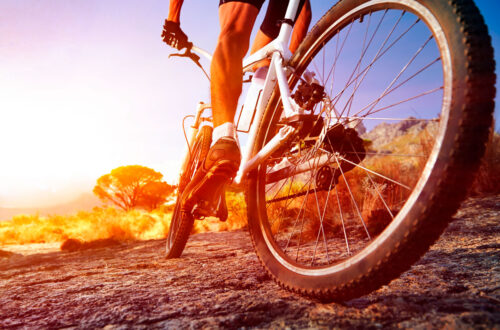 Mann fährt mit einem Mountainbike auf einem unebenen Weg bei Sonnenuntergang, umgeben von Natur und sanften Hügeln.