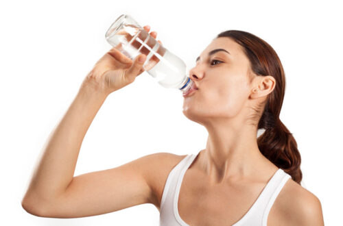 Frau trinkt Wasser aus einer Glasflasche, was auf gesunde Hydration und einen aktiven Lebensstil hinweist.