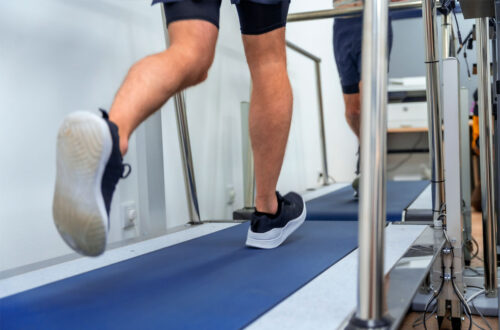 Beine von Sportlern beim Laufen auf einem Laufband in einer modernen Trainingsumgebung. Die Geräte sind mit Handläufen ausgestattet, während die Teilnehmer ihre Fitness verbessern.