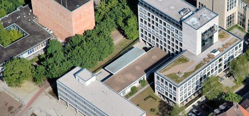 Luftaufnahme eines modernen Verwaltungsgebäudes mit großzügigen Grünflächen und Terrassen, umgeben von Bäumen und einem ruhigen Außenbereich.