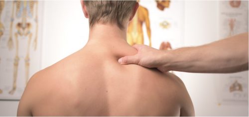 Eine Hand führt eine Massage an den Schultern einer Person durch, während anatomische Diagramme im Hintergrund sichtbar sind. Diese Darstellung zeigt die Anwendung von physikalischer Therapie zur Linderung von Verspannungen im Nacken- und Schulterbereich.